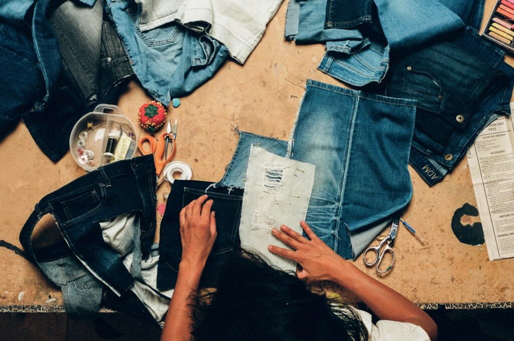 Person sewing denim patches on a table surrounded by sewing tools and denim pieces.